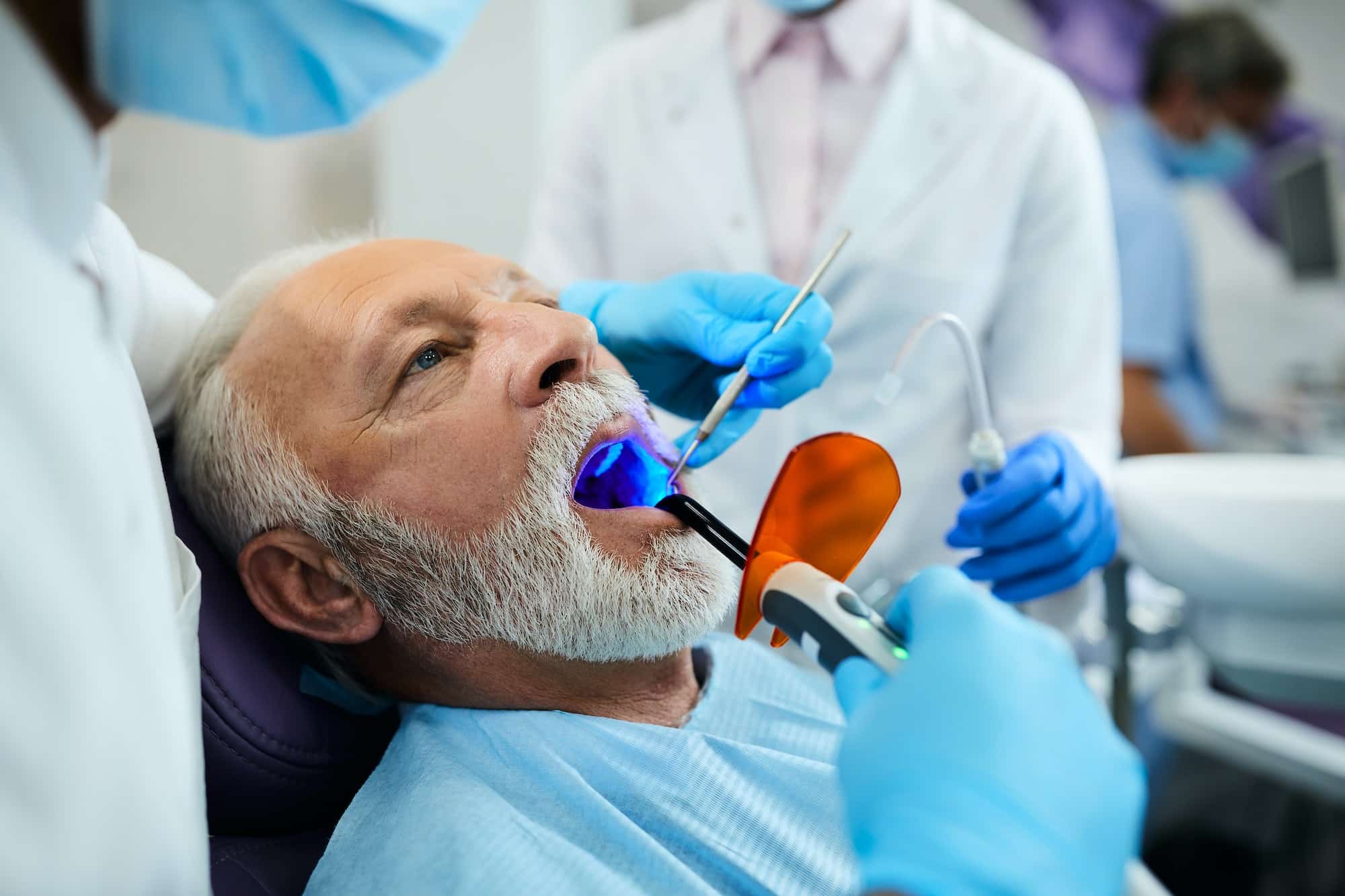 Mature man during dental filling drying procedure with curing UV light at dental clinic.